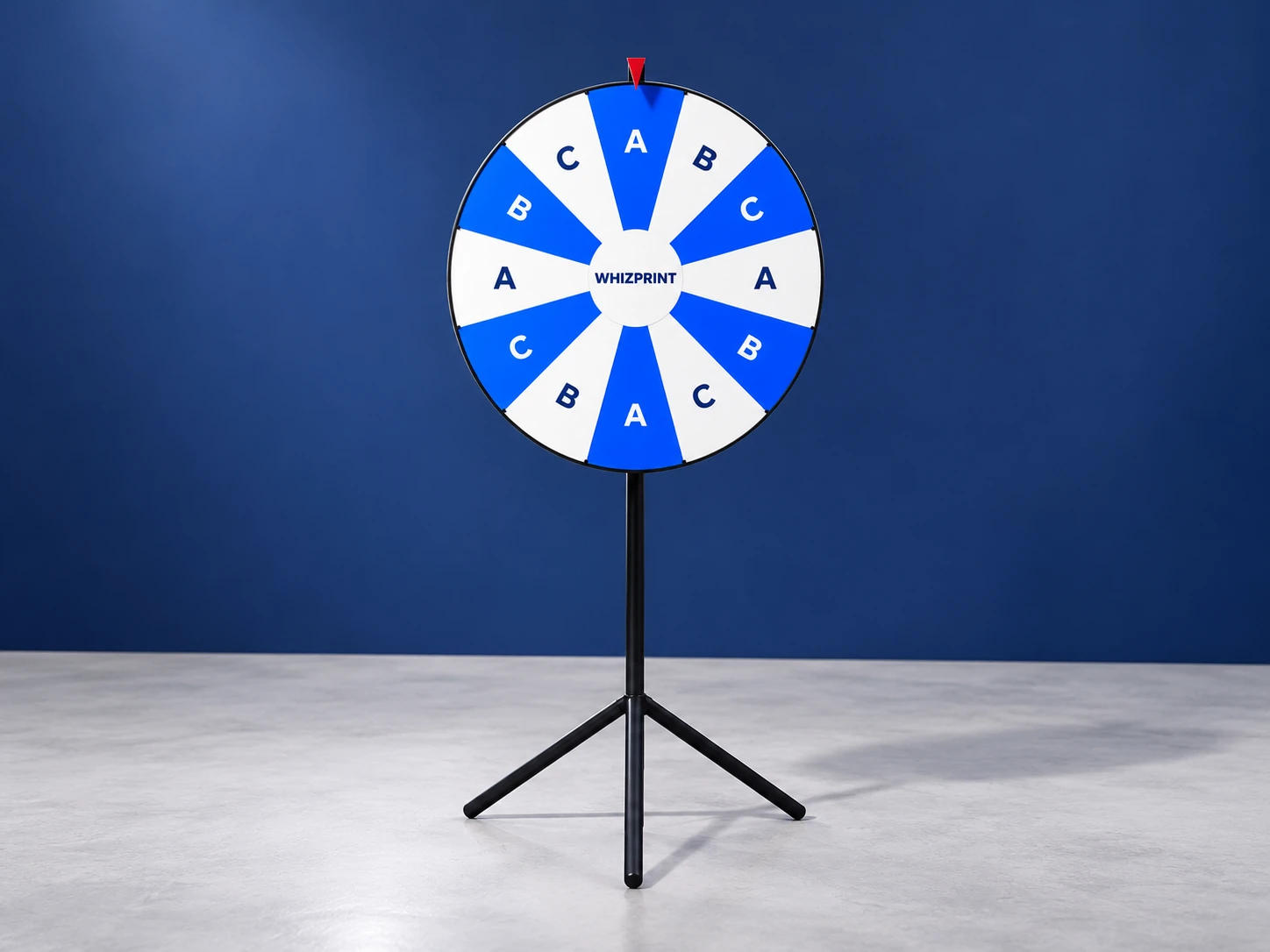 Twelve-section blue and white Whizprint spin wheel on a black tripod stand in an indoor event space.